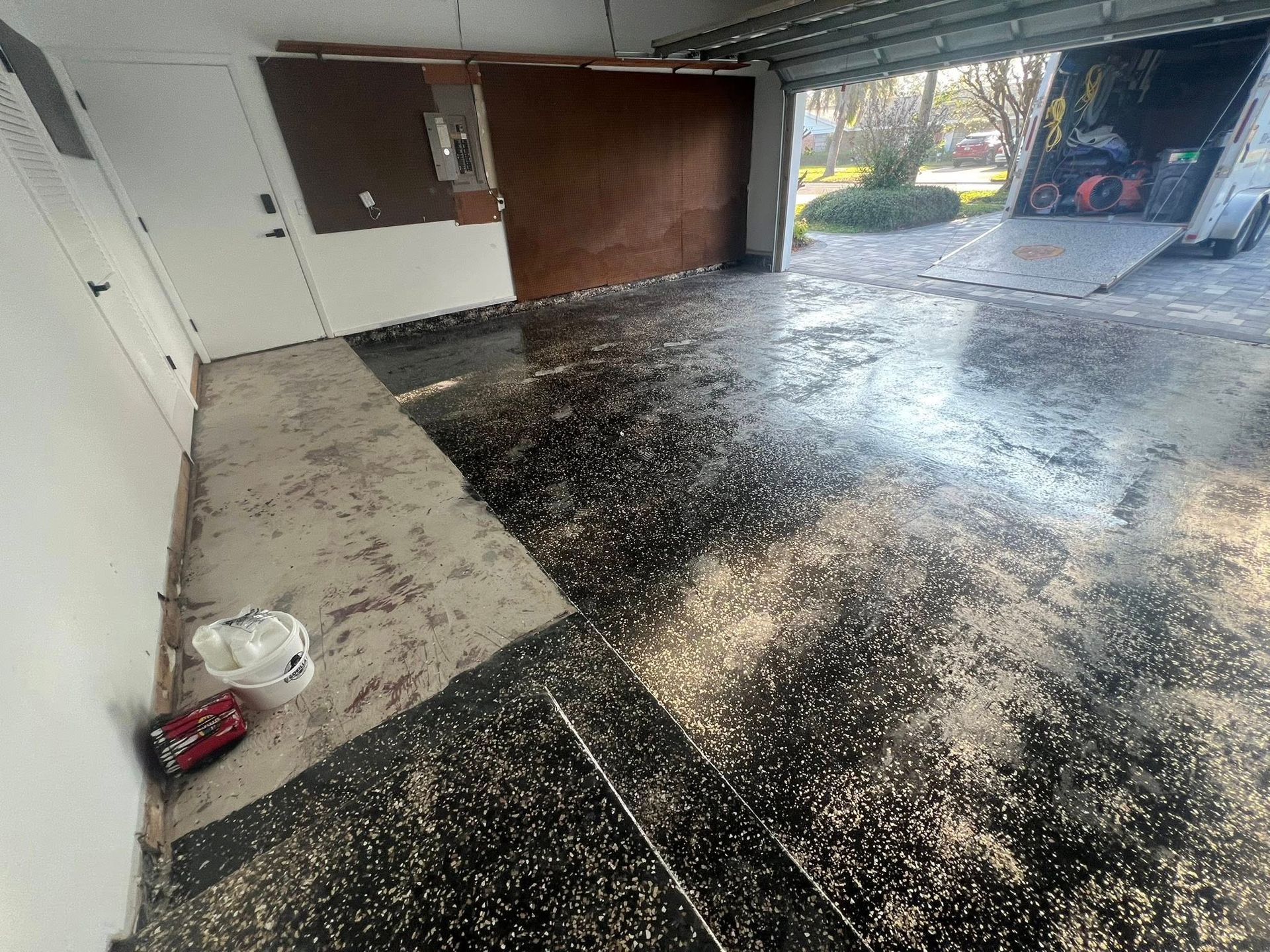 Garage floor covered in debris with an open door and moving truck.
