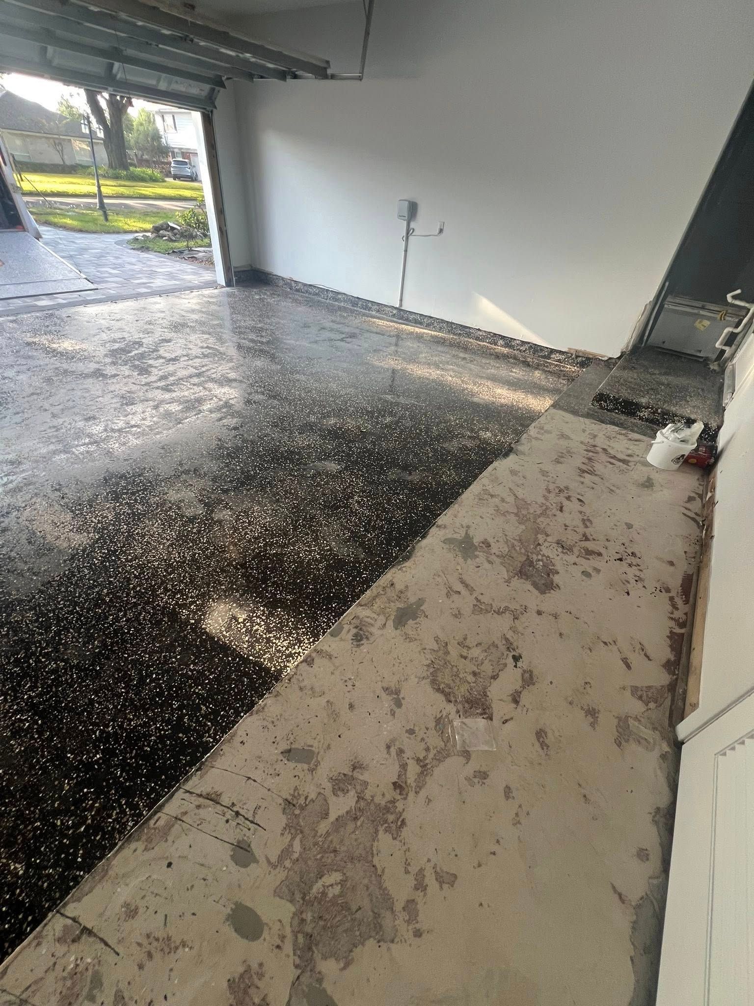 Garage interior with dark speckled flooring and a light-colored concrete ramp leading to the main floor. The garage door is open.