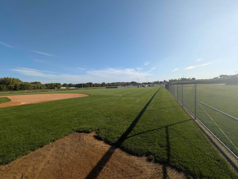 Baseball field with green grass, blue sky, and a chain-link fence.