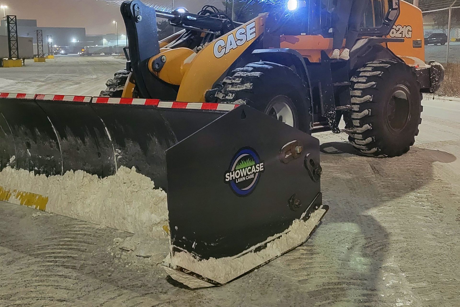 Yellow CASE snowplow clearing snow on a parking lot at night.