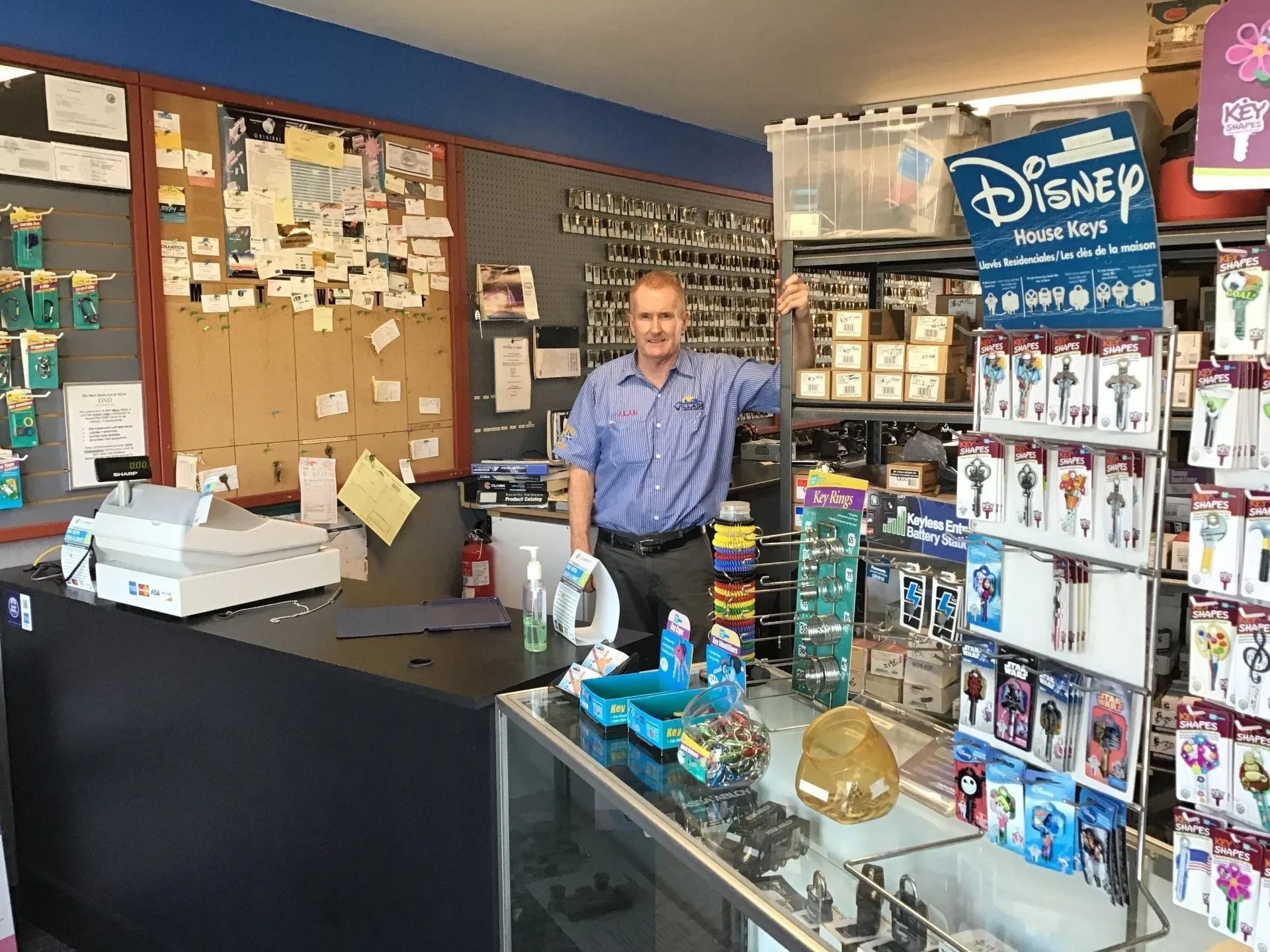 Man in a locksmith shop, standing behind a counter with keys and keychains.