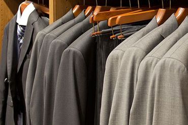 Learn More About Pick Up and Delivery Row of gray suits on wooden hangers in a clothing store closet