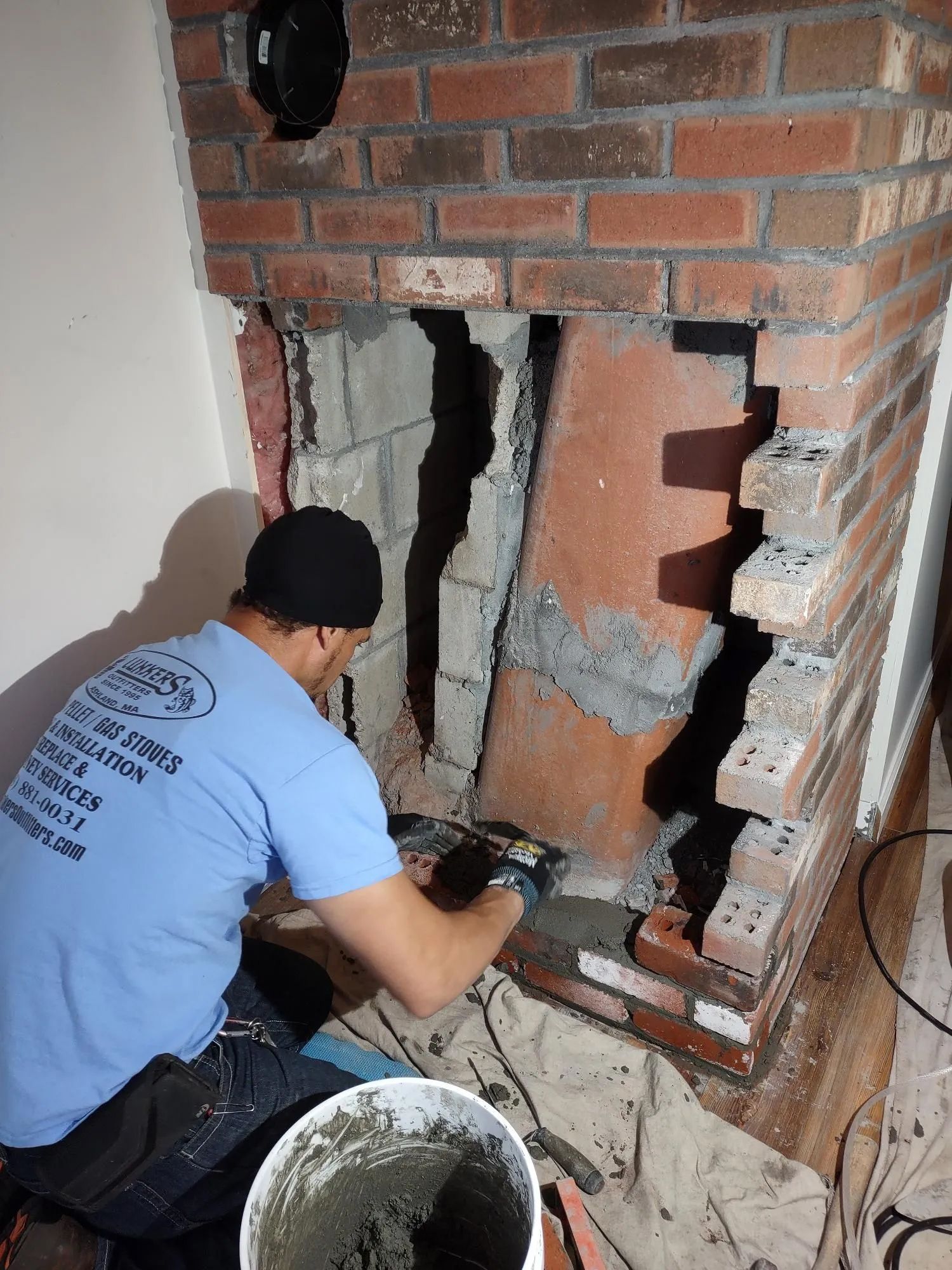 A man in a blue shirt is working on a brick fireplace.