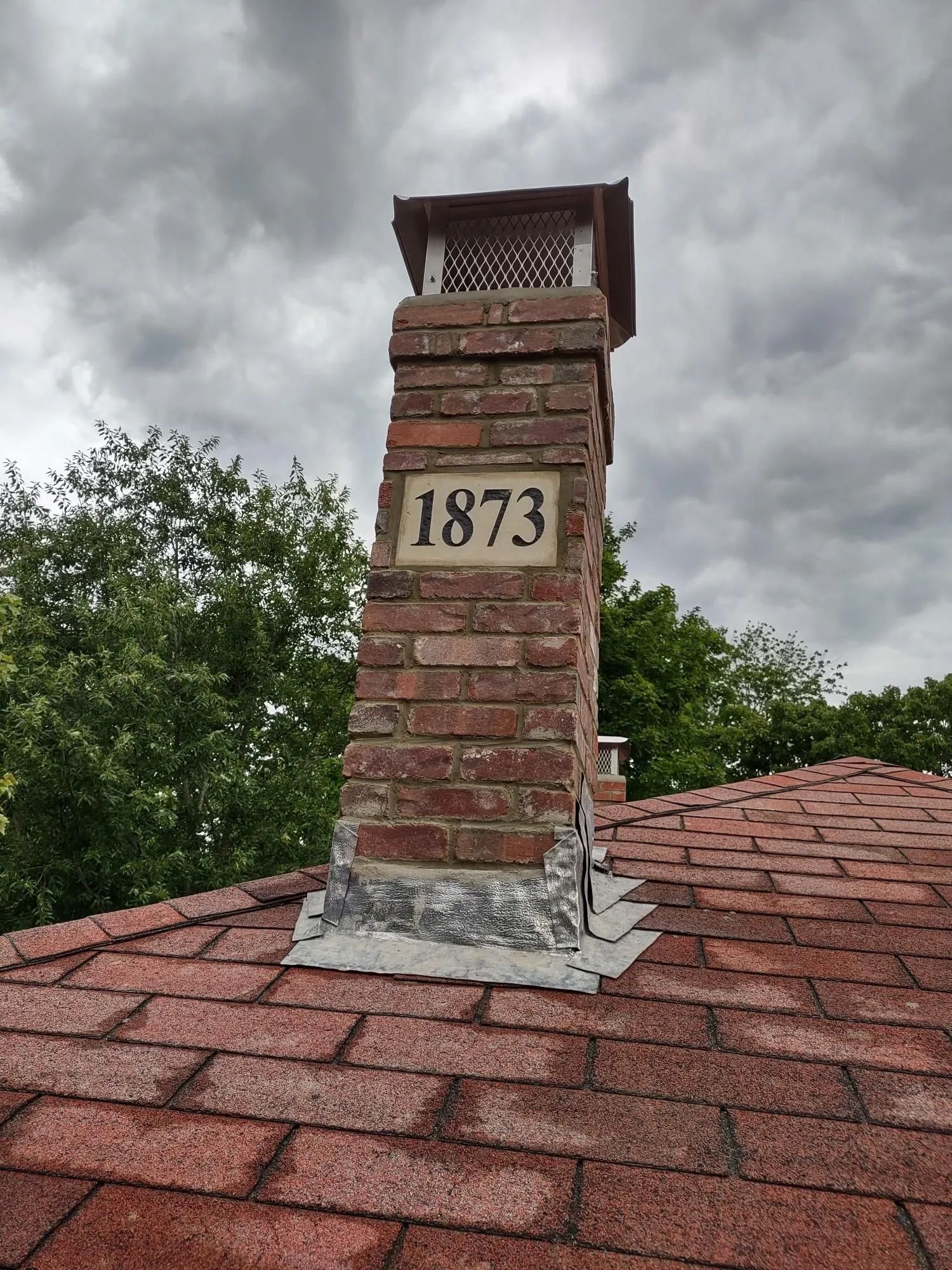 A brick chimney on top of a roof with the number 1873 on it.