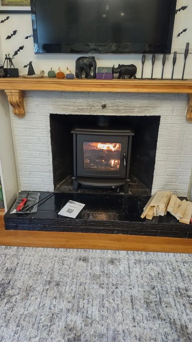 A wood stove is sitting in a fireplace next to a television.