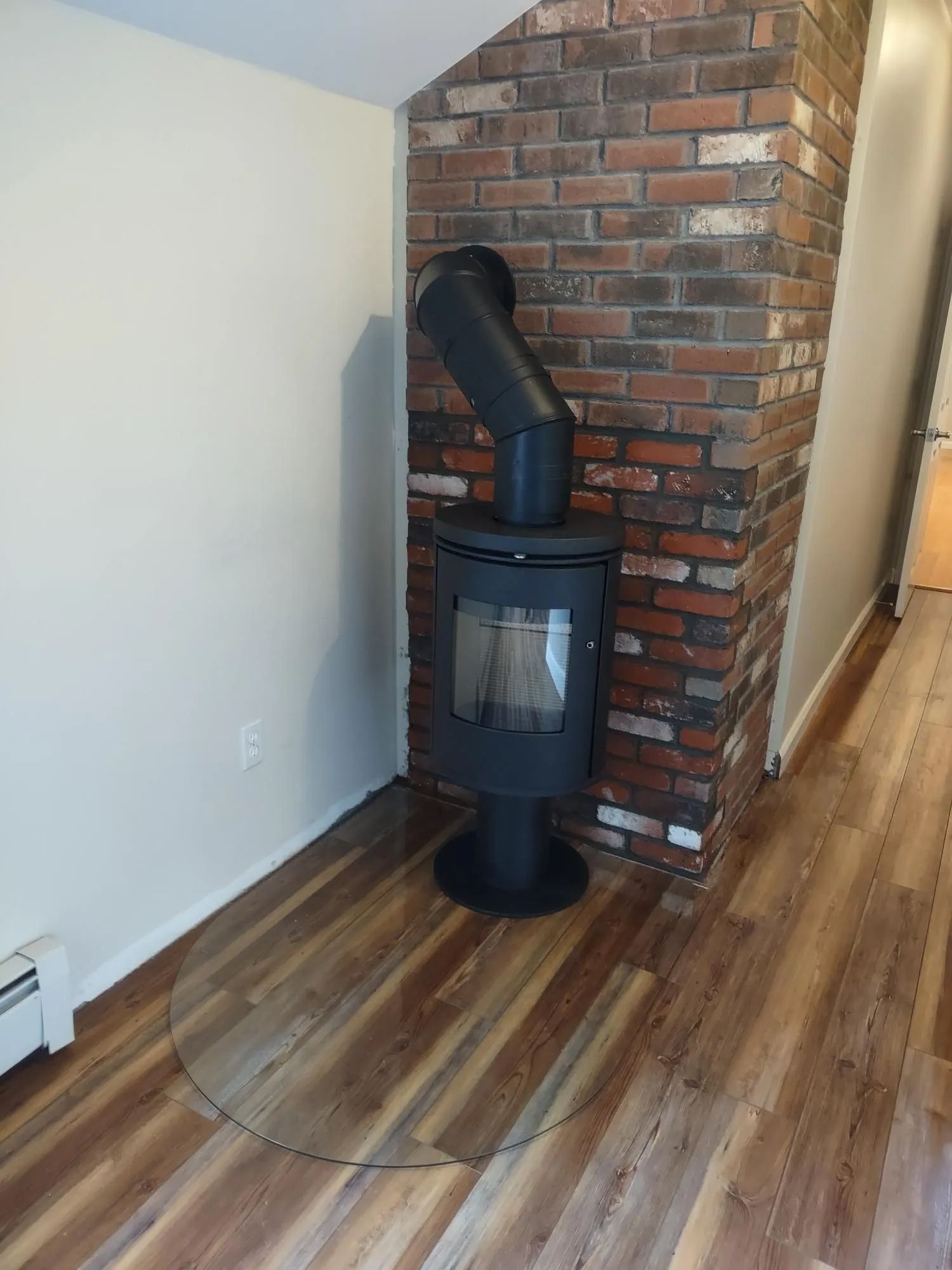 A wood stove is sitting in the corner of a room next to a brick wall.