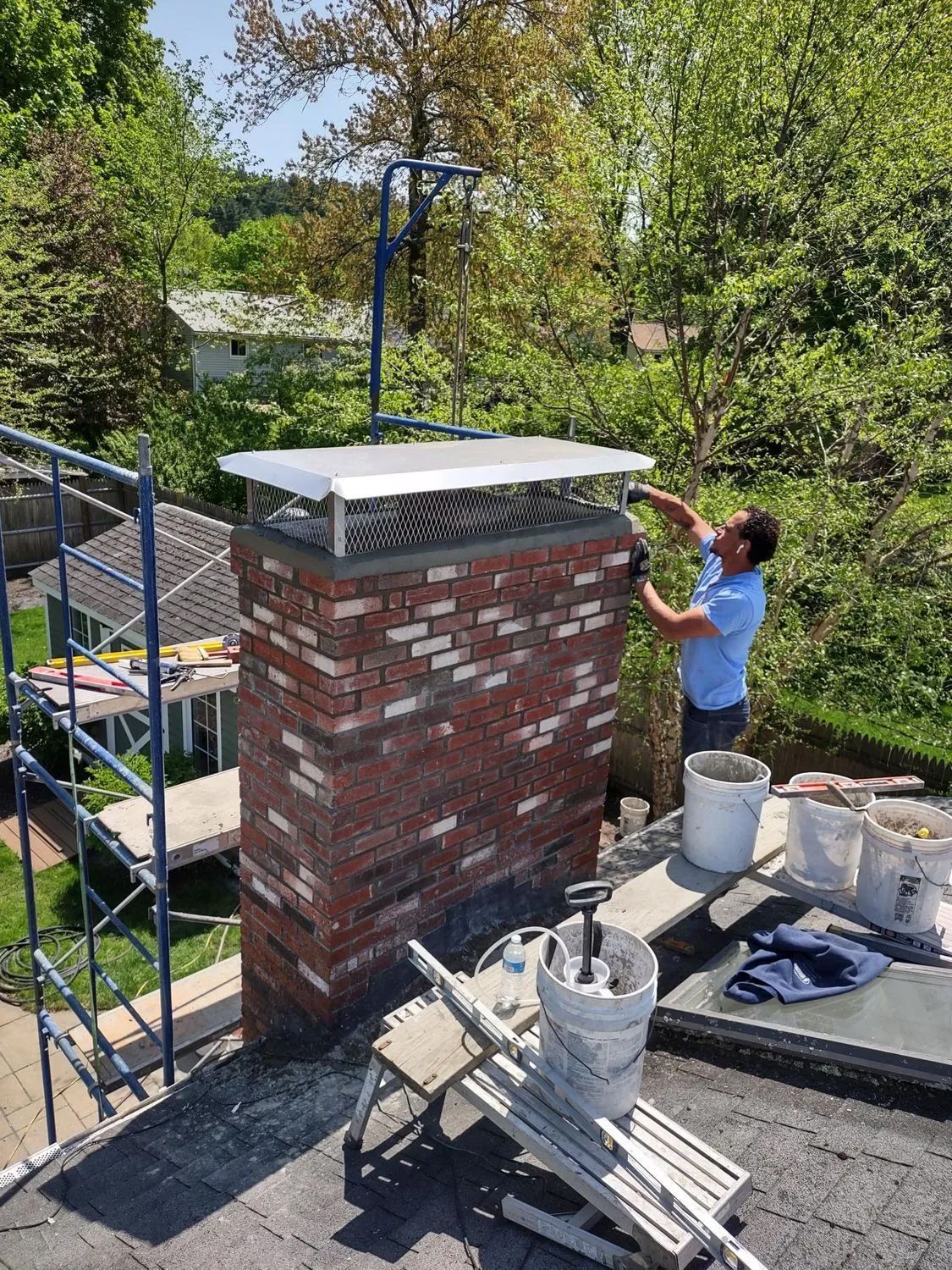 A man is working on a brick chimney on top of a roof.
