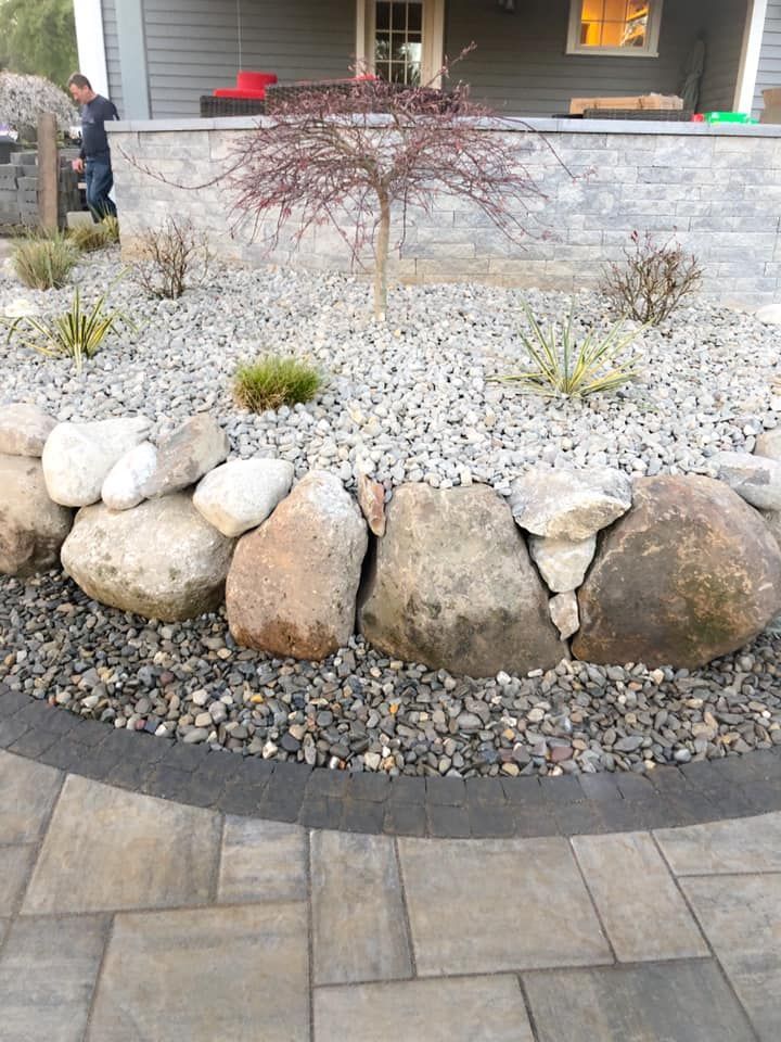 A rock garden with a tree in the middle of it in front of a house.