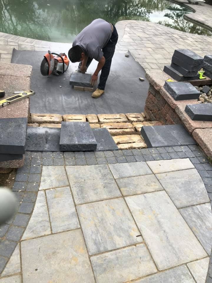 A man is laying bricks on a patio next to a pool