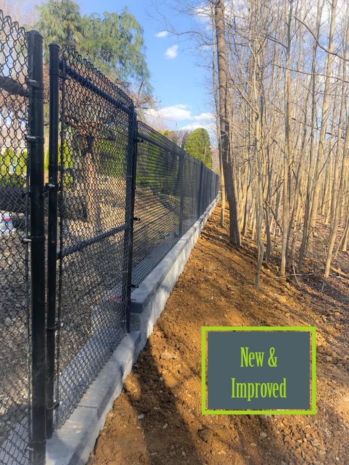 A chain link fence with a gate is surrounded by trees and dirt.