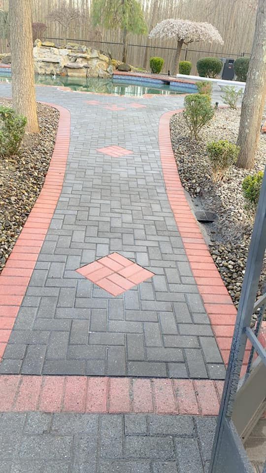 A brick walkway leading to a pool in a backyard.