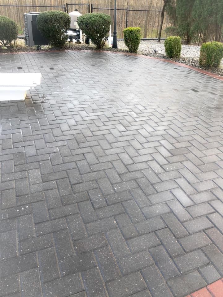 A brick driveway with a bench and bushes 