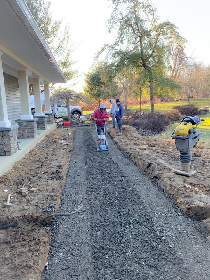 A man is working on a gravel driveway in front of a house