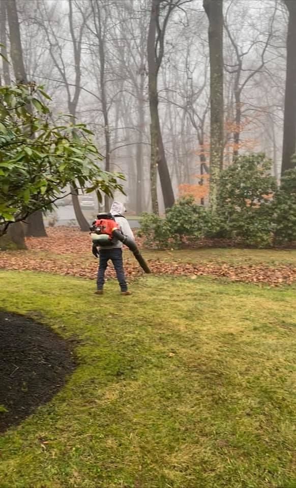 A man is blowing leaves in a backyard on a foggy day.