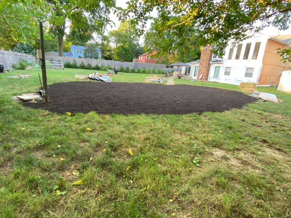 A large pile of mulch is sitting in the middle of a lush green yard