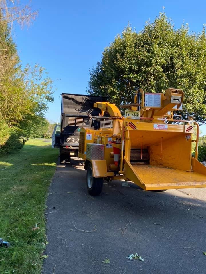 A yellow tree chipper is parked on the side of the road next to a truck