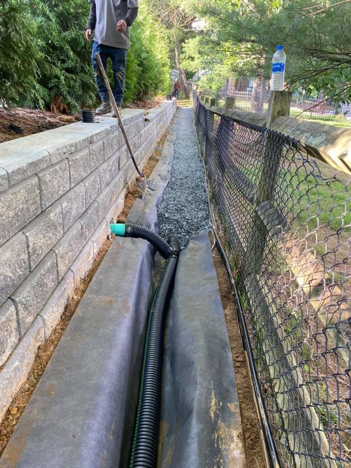 A man is standing next to a drain with a hose attached to it.