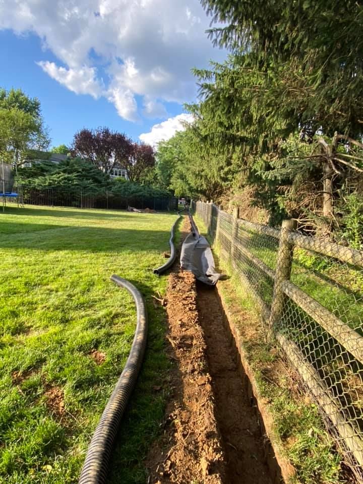 A man is digging a trench in a yard next to a wooden fence.