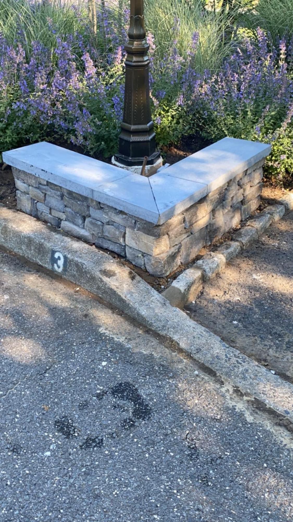 A stone bench is sitting on the side of the road next to a lamp post.