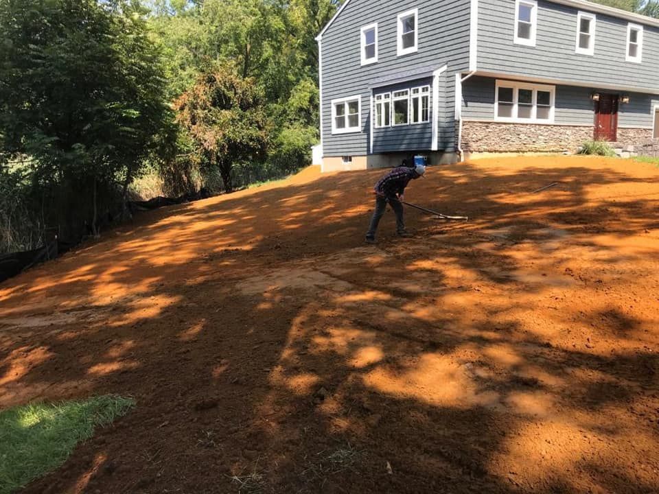 A man is standing in a dirt field in front of a house.