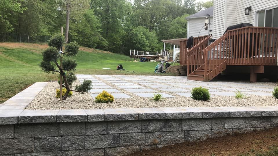 A patio with a wooden deck and a stone wall in front of a house