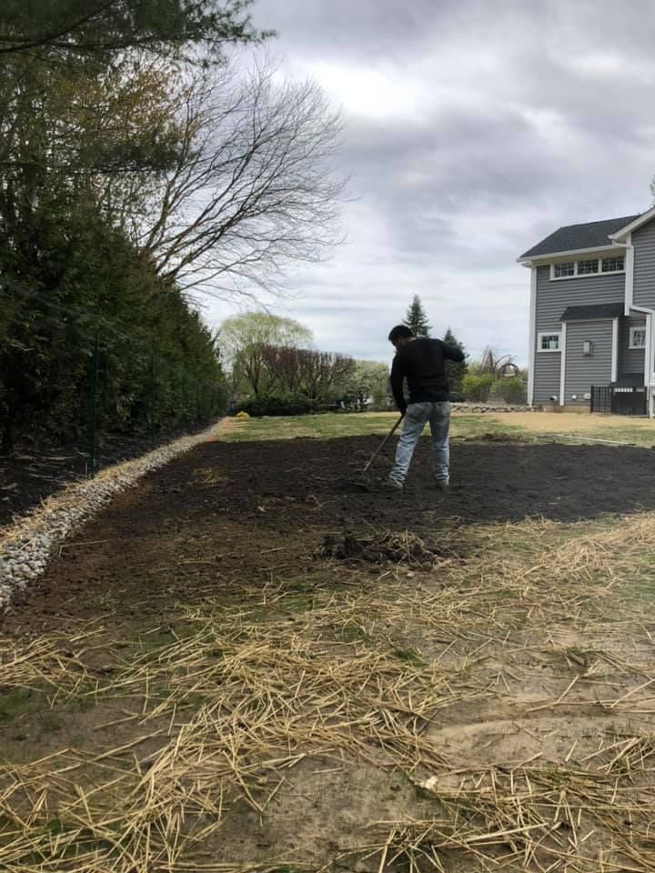 A man is raking dirt in a yard in front of a house