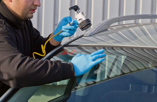Technician using a spray gun to coat a car windshield with protective film