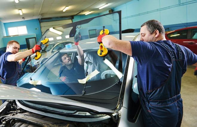 Two mechanics using suction tools to remove a windshield in a workshop
