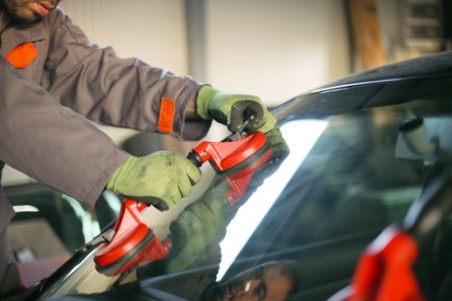 Worker polishing a car windshield with a red buffer and green gloves in a garage