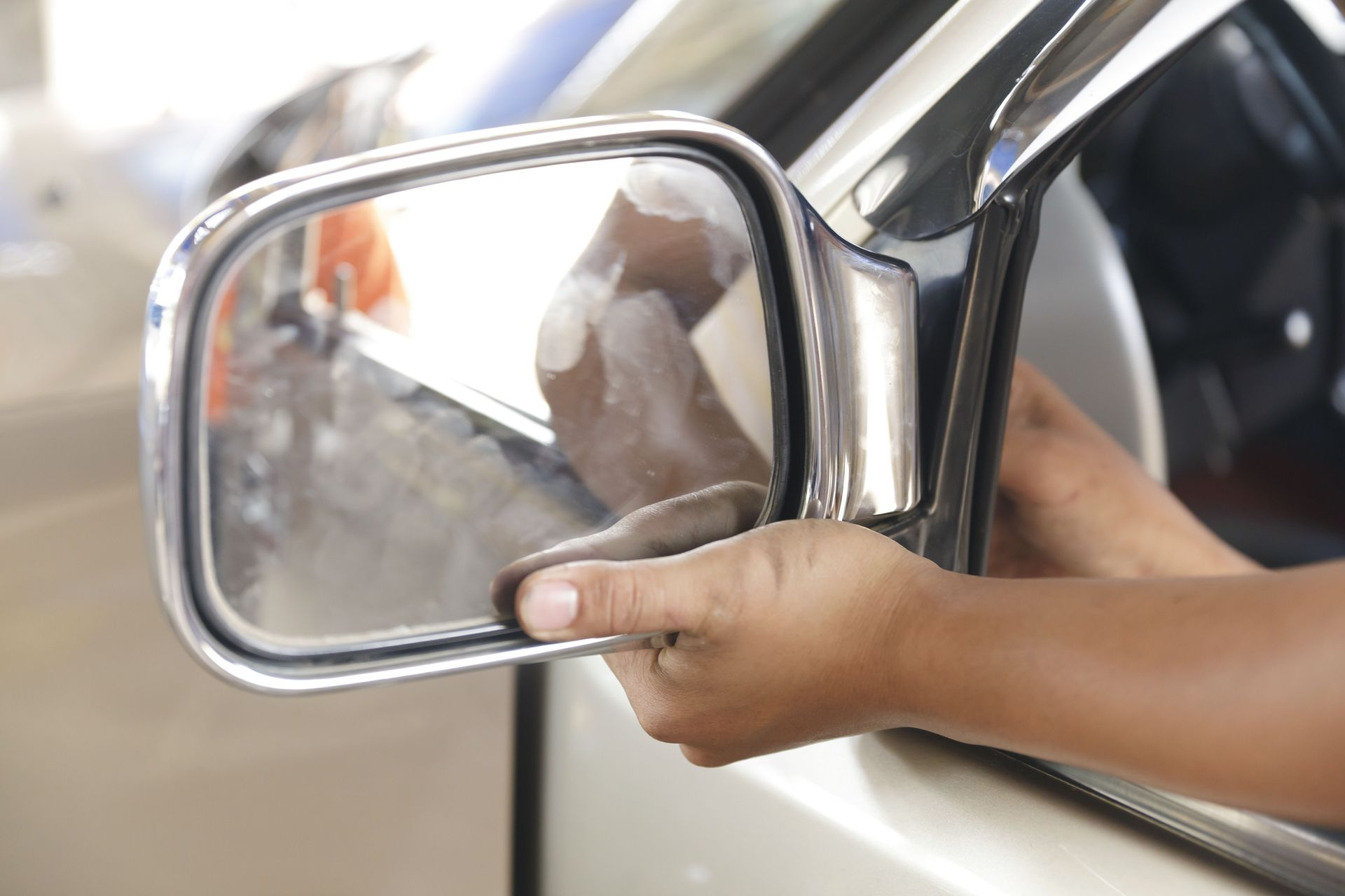 Hand adjusting a car’s side mirror on a beige vehicle