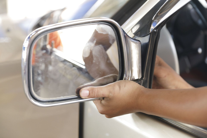 Hand adjusting a car’s side mirror on a beige vehicle