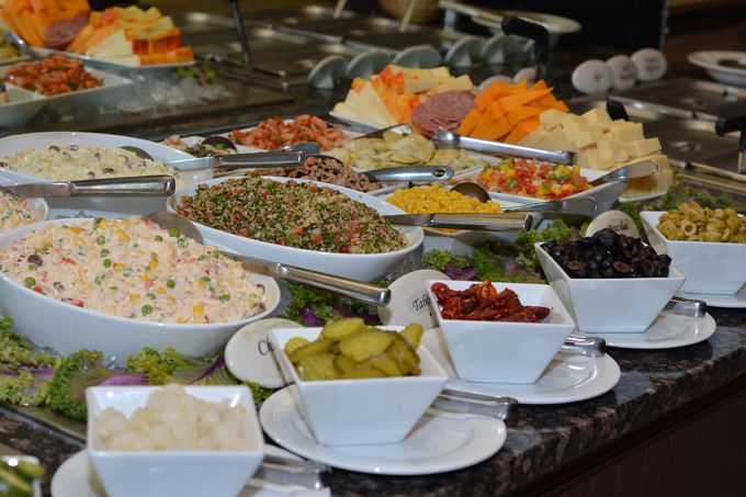 Self-serve salad bar with trays of vegetables, cheeses, and toppings under glass display