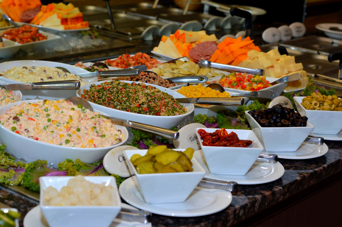 Self-serve salad bar with trays of vegetables, cheeses, and toppings under glass display