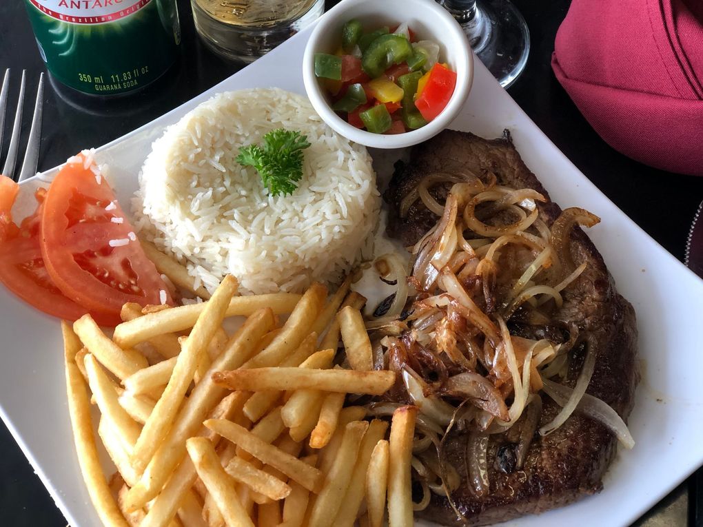 Grilled steak with rice, fries, and a small Brazilian flag on a square white plate.