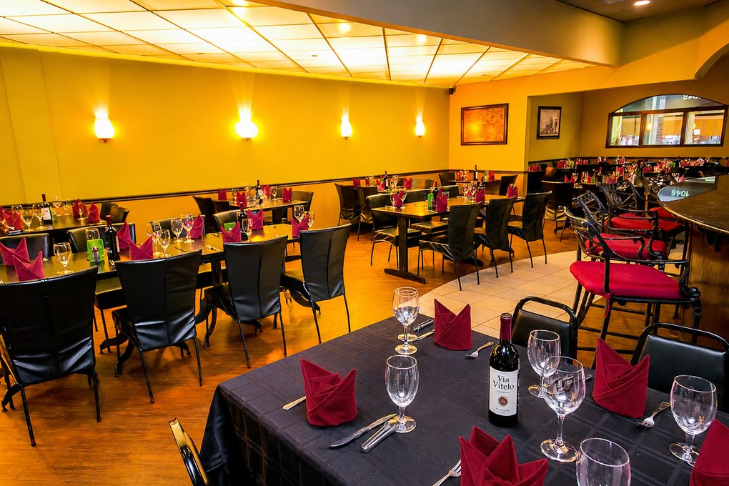 Dimly lit restaurant dining room with set tables, red napkins, wine glasses, and wall art