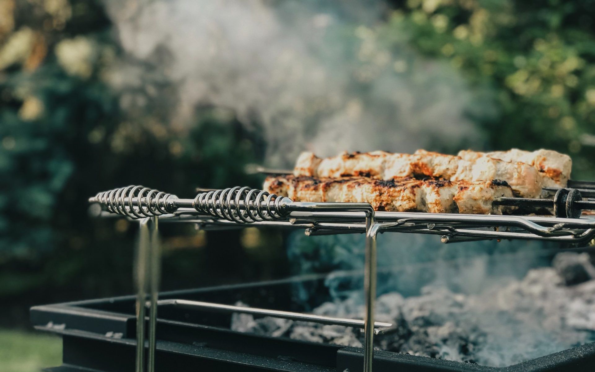 Skewered meat grilling over open flames with smoke rising outdoors