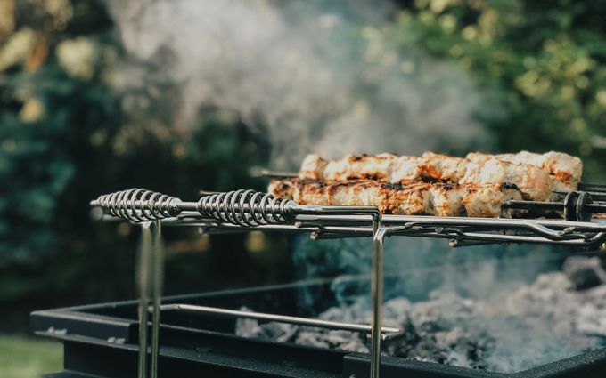 Skewered meat grilling over open flames with smoke rising outdoors