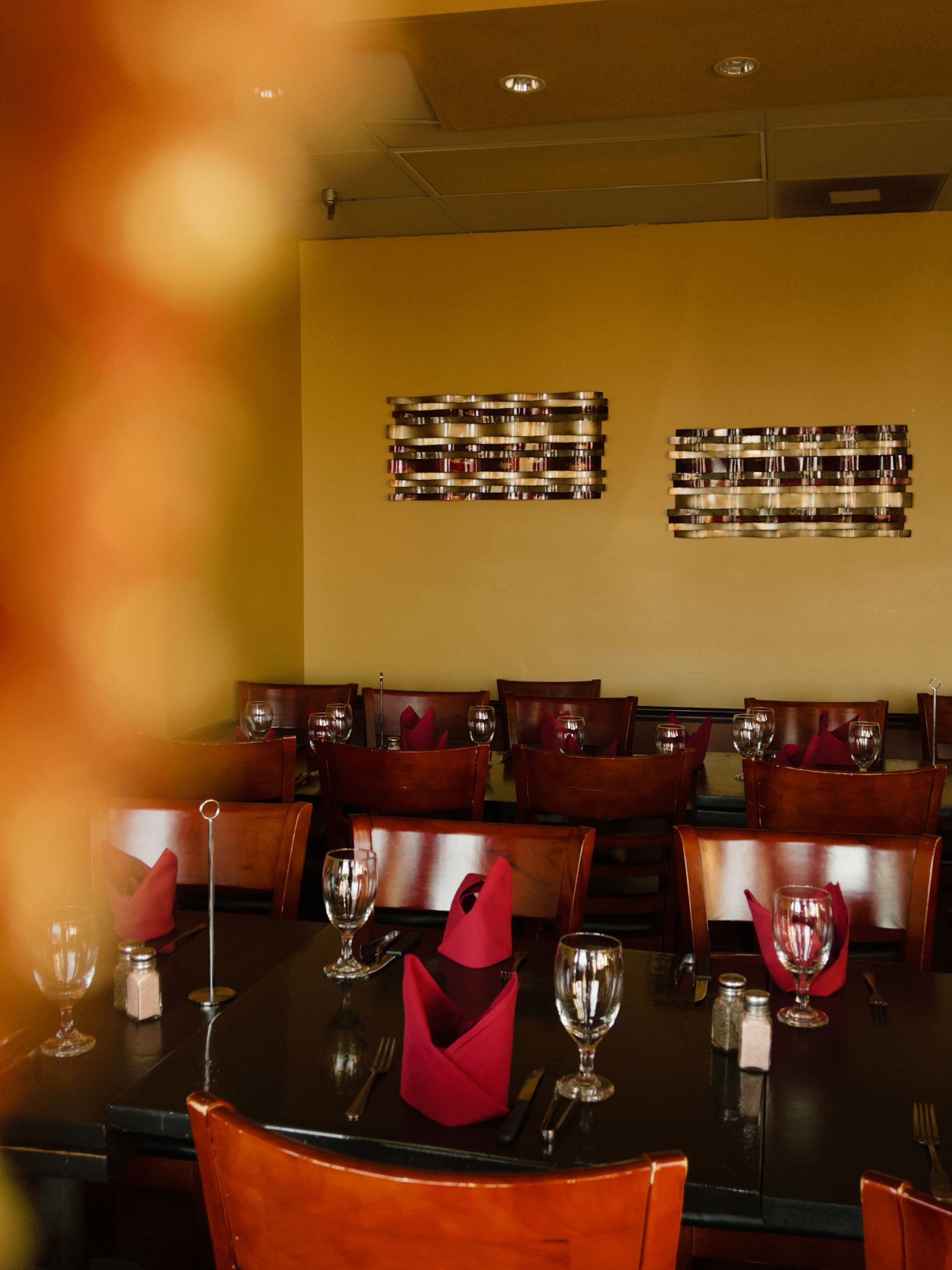 Dimly lit restaurant dining room with set tables, red napkins, wine glasses, and wall art