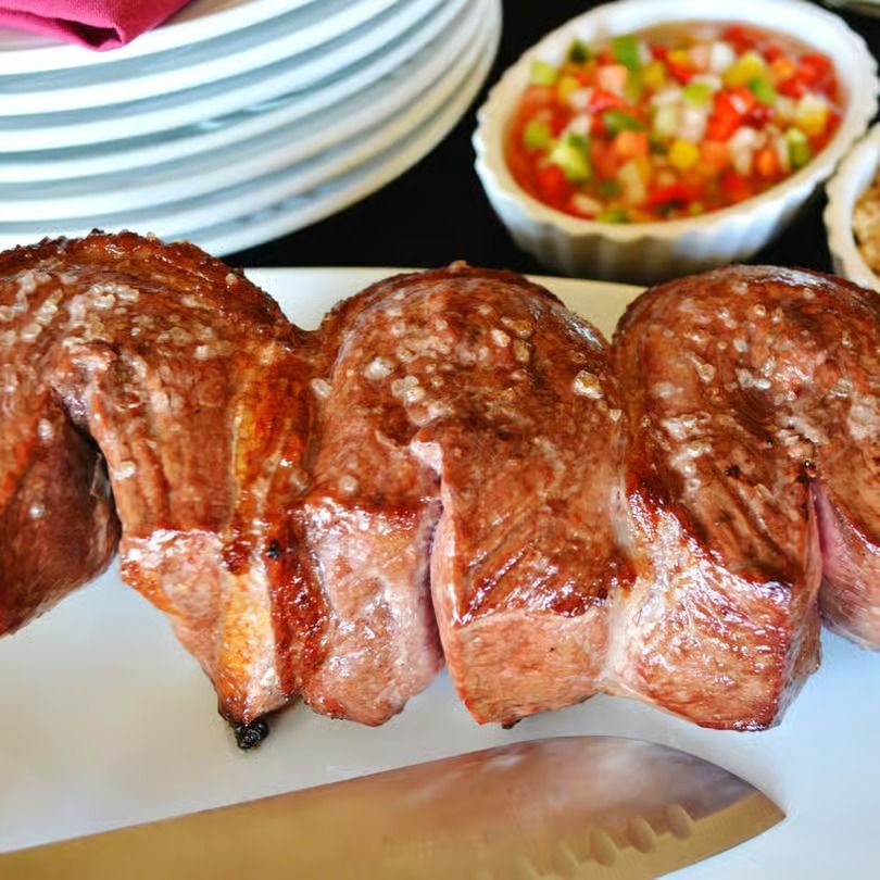 Sliced grilled steak on a cutting board with a knife and a bowl of salsa in the background