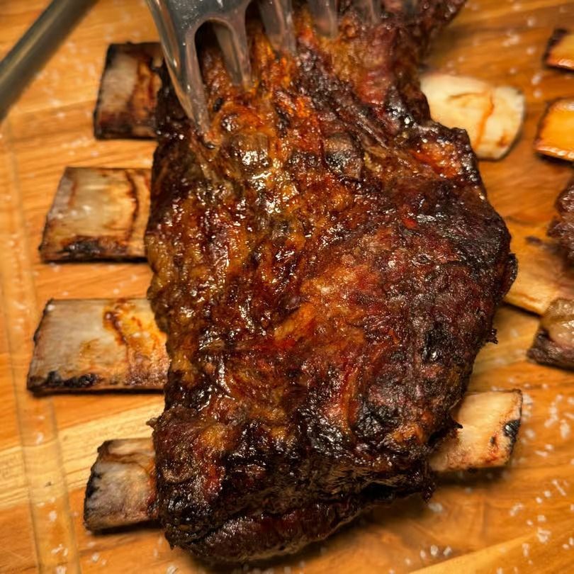 Grilled rack of ribs with dark charred glaze on a wooden cutting board