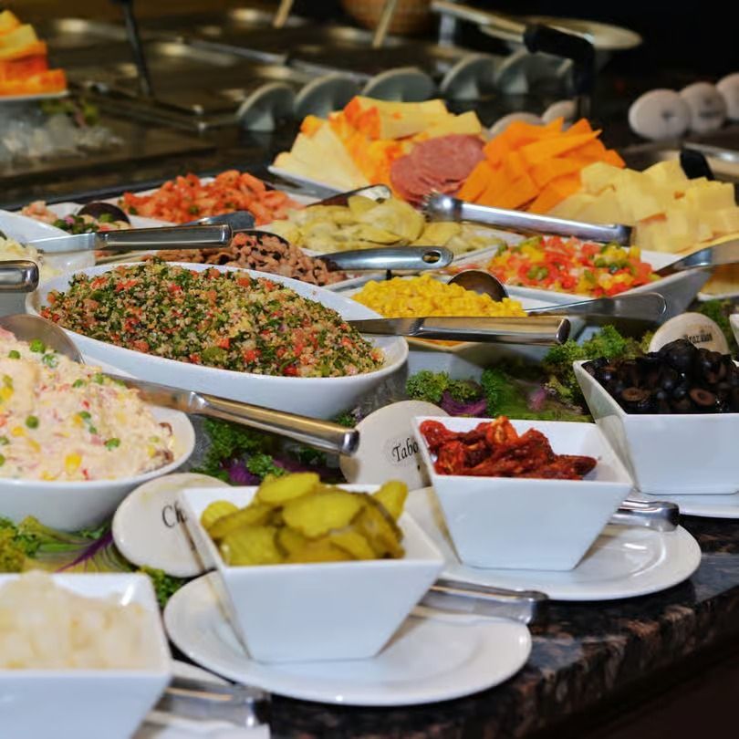 Buffet table with assorted salads, olives, pickles, and cheese trays in serving dishes