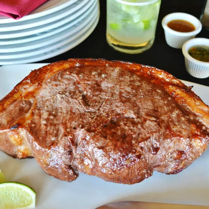 Grilled steak on a white plate with lime wedges, sauces, and stacked plates in the background