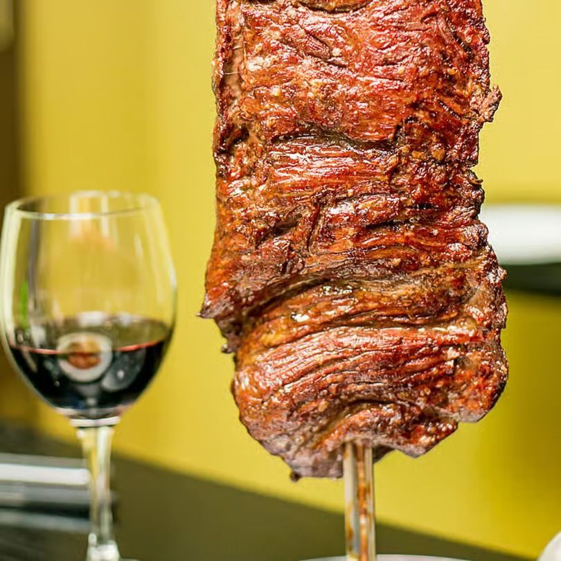 Glazed roast meat on a spit beside a glass of red wine