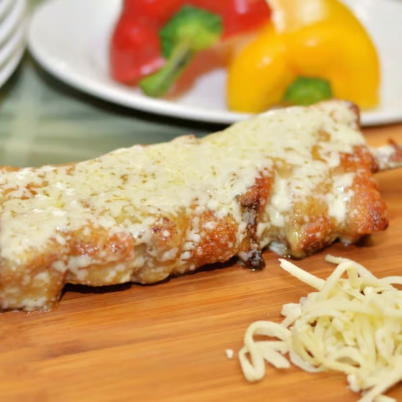 Cheesy baked enchilada on a wooden board with bell peppers in the background