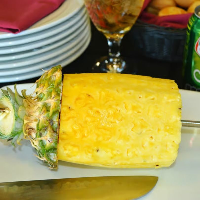 Peeled pineapple on a table with stacked plates and a knife beside it
