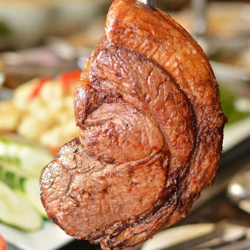 Close-up of a grilled steak slice on a plate with blurred vegetables in the background