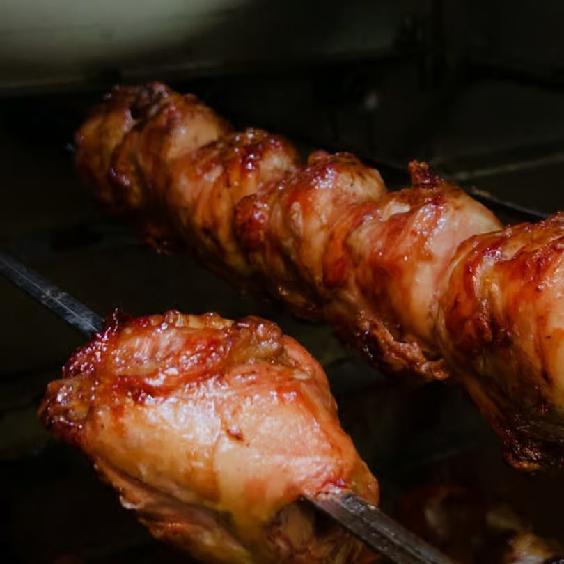 Glazed chicken pieces roasting on metal skewers over a grill