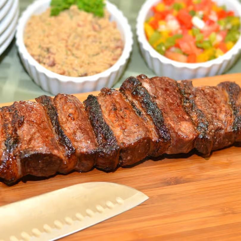 Grilled sliced steak on a cutting board with a serving knife, side dishes blurred in the background