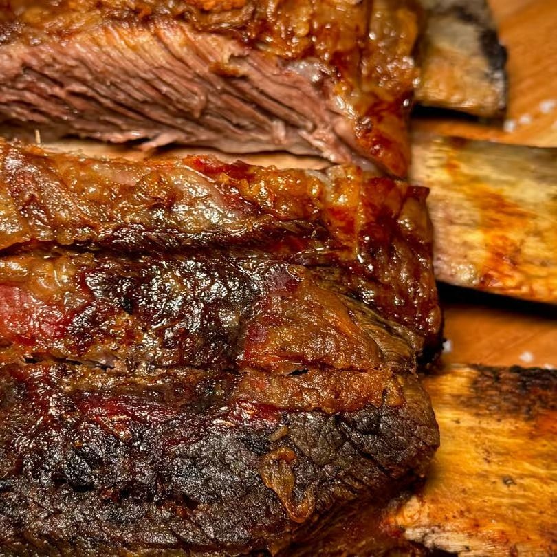 Close-up of grilled meat with a charred crust on wooden skewers, showing juicy sliced interior.
