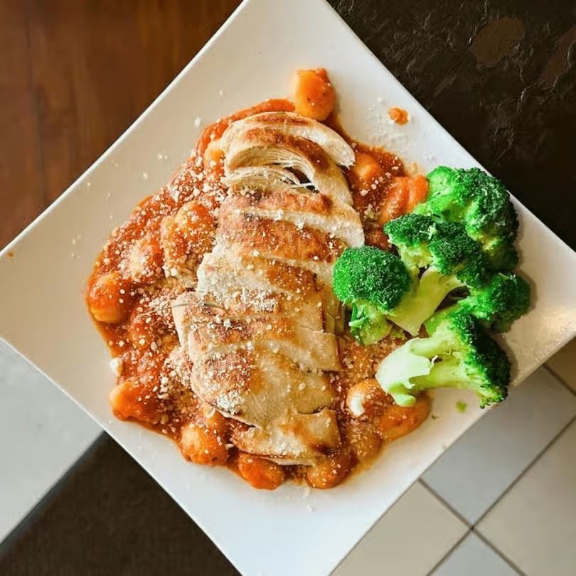 Plated chicken parmesan with red sauce, melted cheese, and broccoli on a white square plate